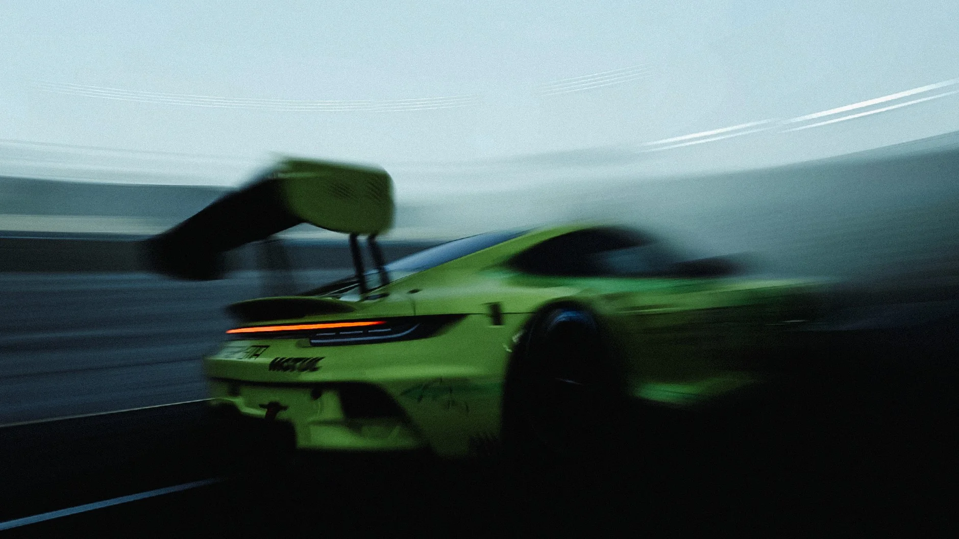 Green race car with a large rear wing, blurred with speed on a track