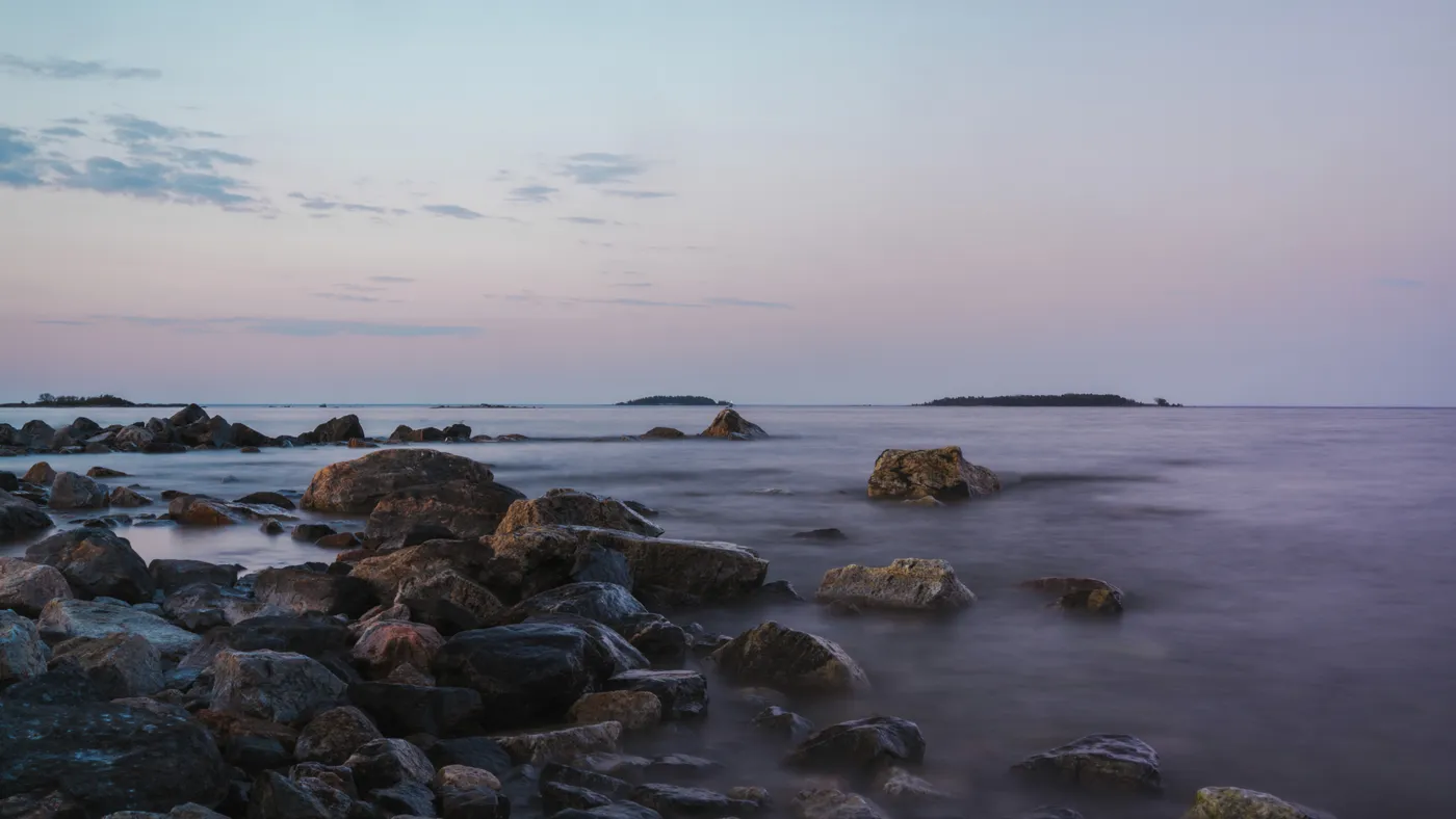 Long exposure of a calm sea over a rocky shoreline at dusk