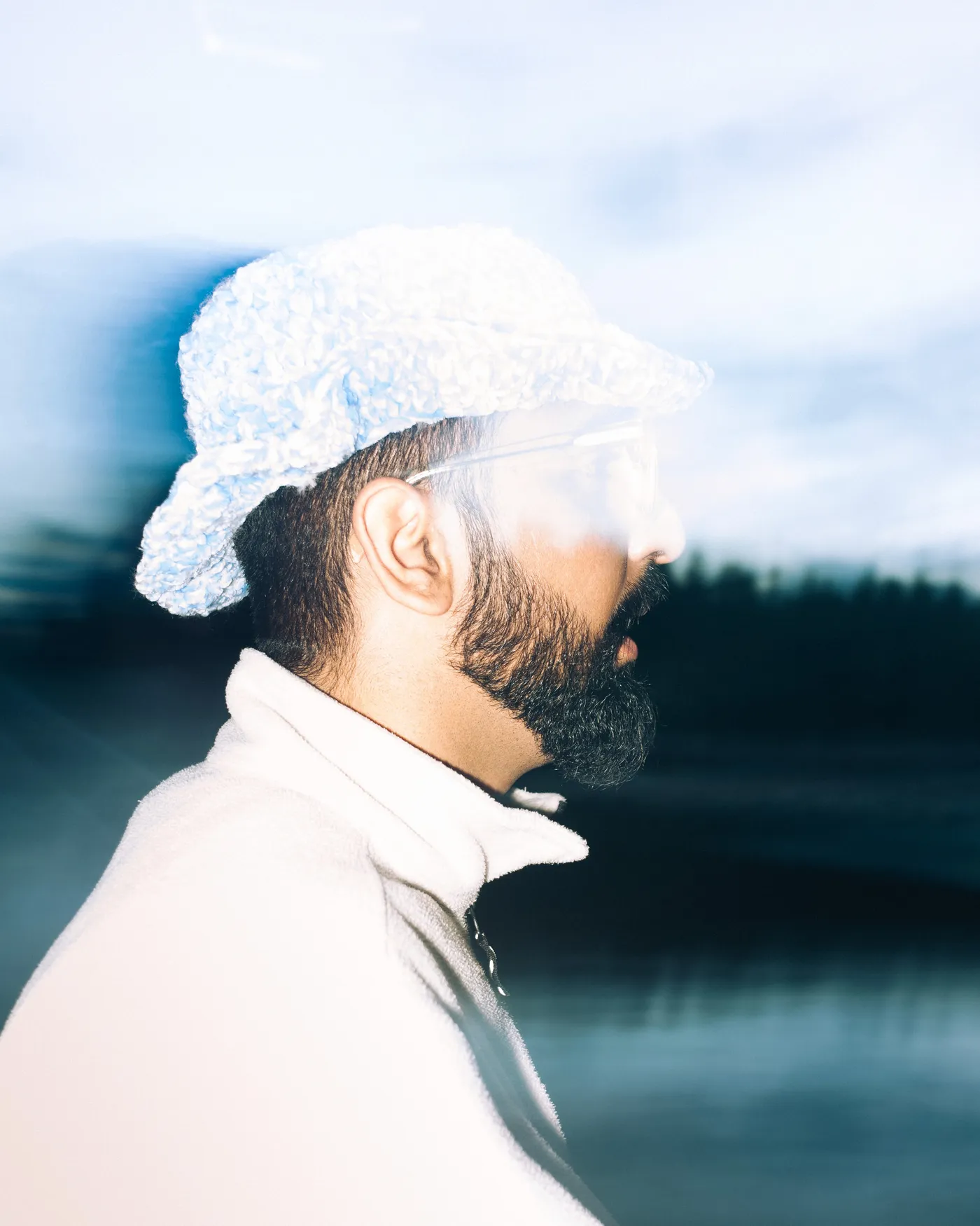 Side profile of a bearded man in a white bucket hat by a lake